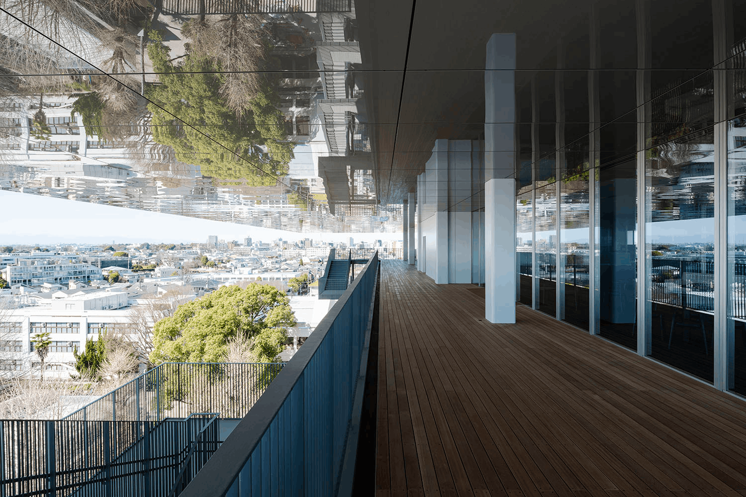画像：多摩美術大学 上野毛キャンパス 本部棟5F外観_昼景／本部棟の大屋根の下の開放的なテラスは、雨風をしのげる安心感とともに、世田谷の街並みを享受できる。